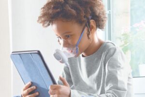 Bambino che utilizza un aerosol Pic Solution per il benessere delle vie respiratorie mentre guarda un tablet.