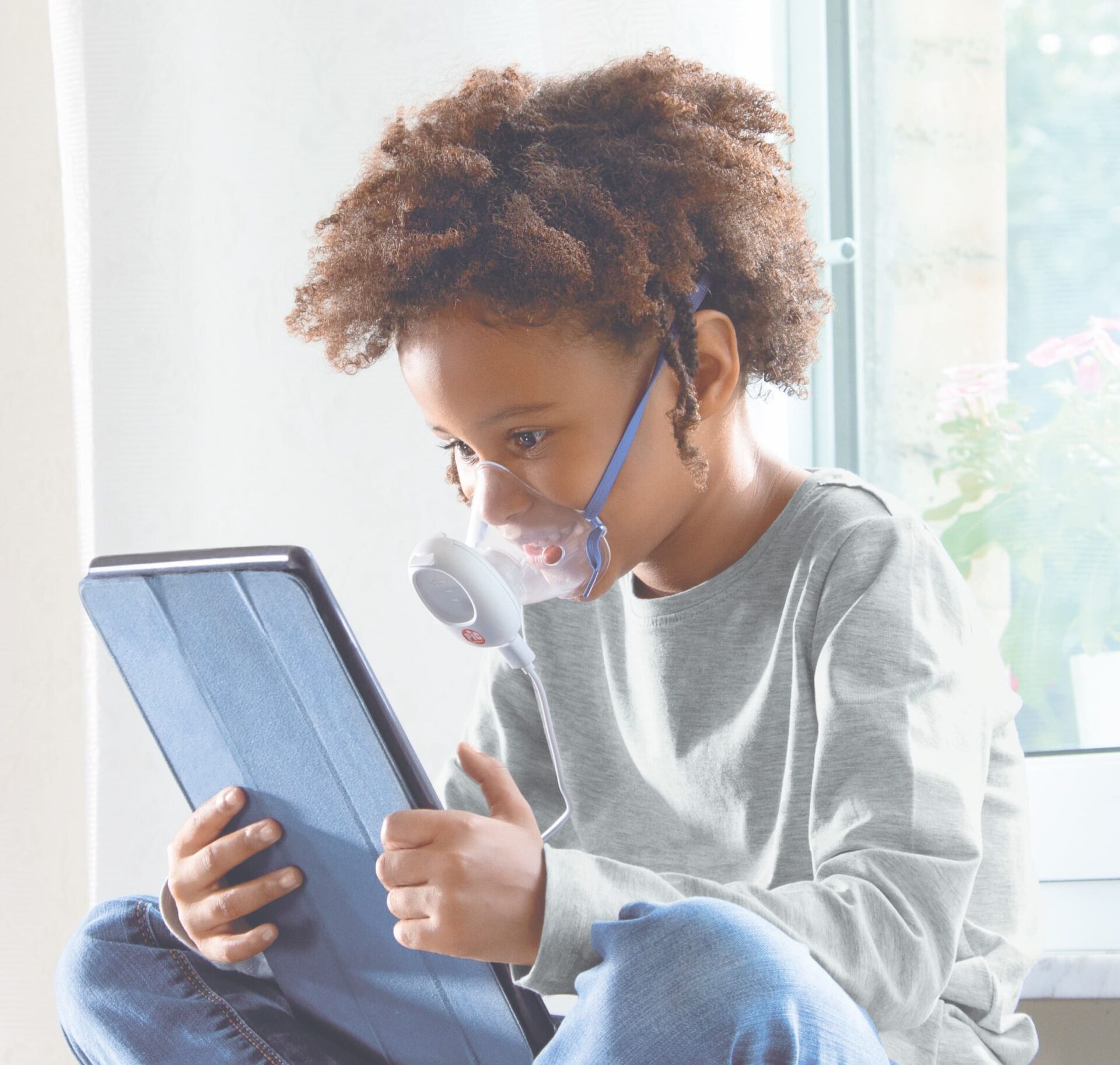 Bambino che utilizza un aerosol Pic Solution per il benessere delle vie respiratorie mentre guarda un tablet.