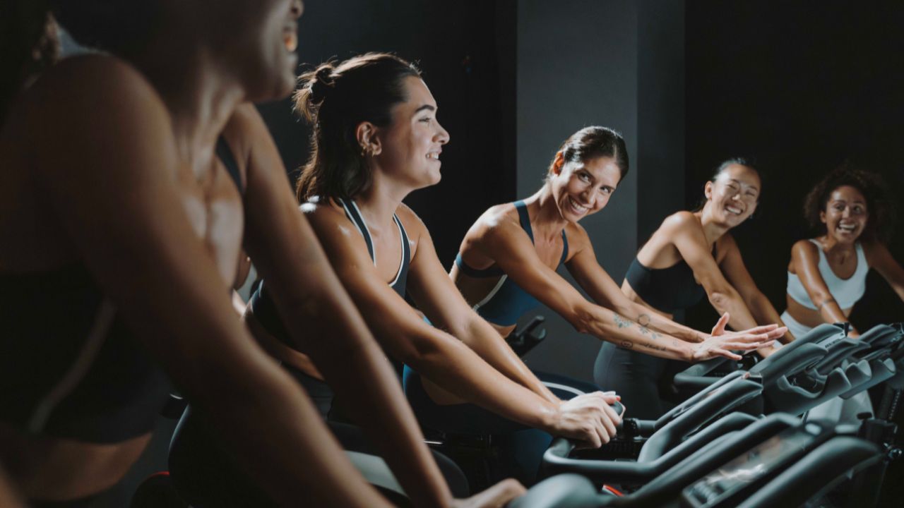 Un gruppo di donne sorridenti durante una sessione di indoor cycling, parte della Oysho Community, che mostra energia e spirito di squadra in palestra