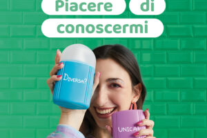 Donna sorridente tiene in mano due confezioni di detergente intimo con le scritte 'Diversa?' e 'Unica!' davanti a uno sfondo verde, promuovendo la campagna 'Piacere di Conoscermi' di Chilly